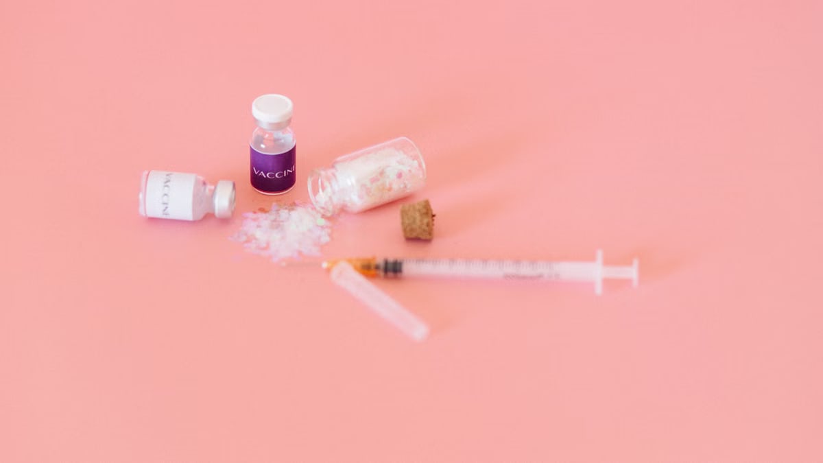 Conceptual image of vaccine vials and syringe on a soft pink background.